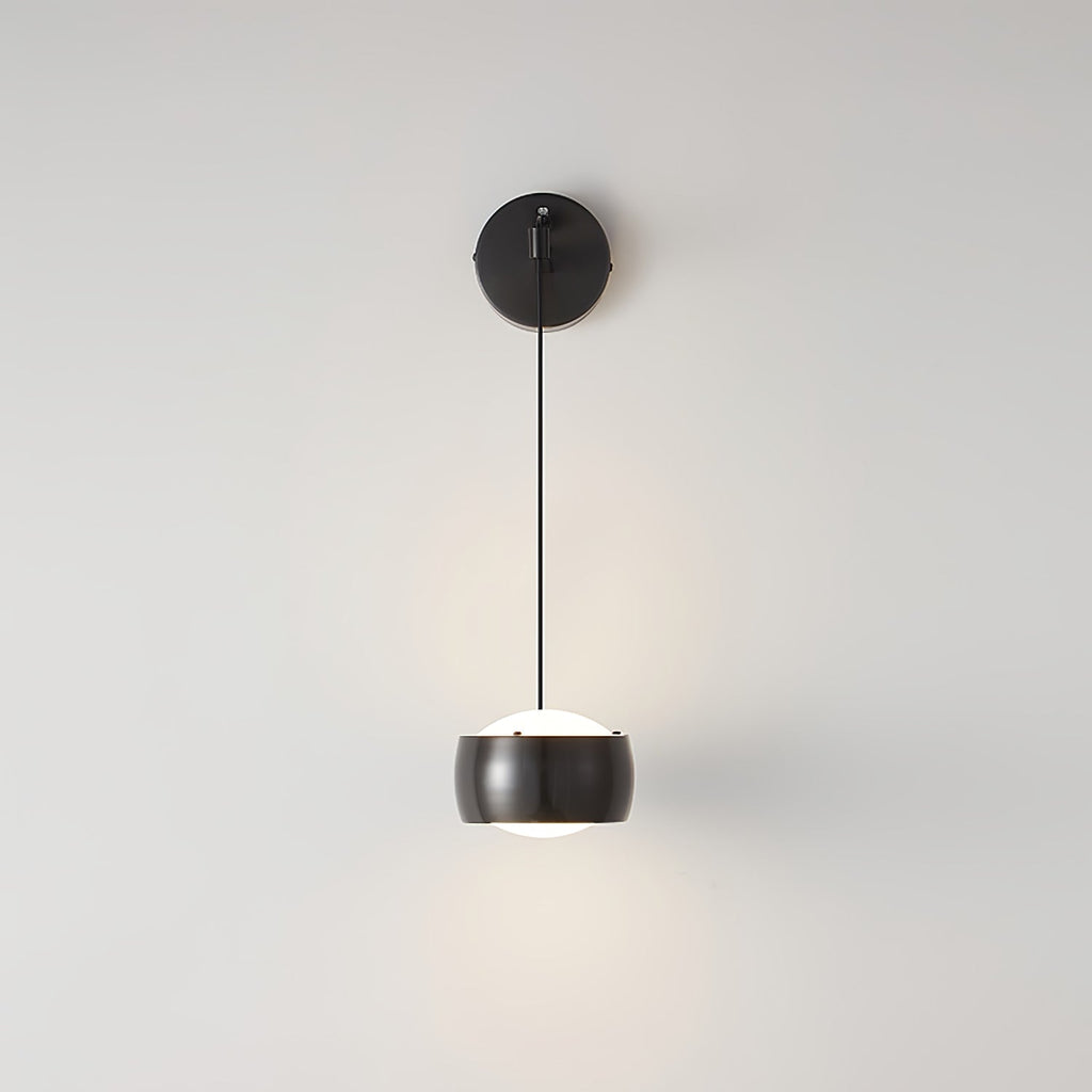 Front view of a black Clérachic wall light on a light grey wall, its shade lit white underneath and a round backplate above.