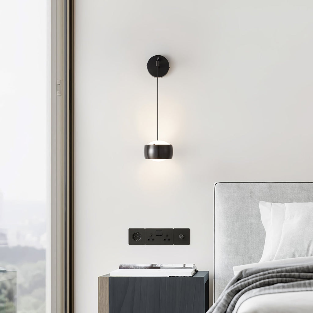 Black Clérachic wall light on a white wall by a floor-to-ceiling window, above a dark bedside cabinet and wall sockets.