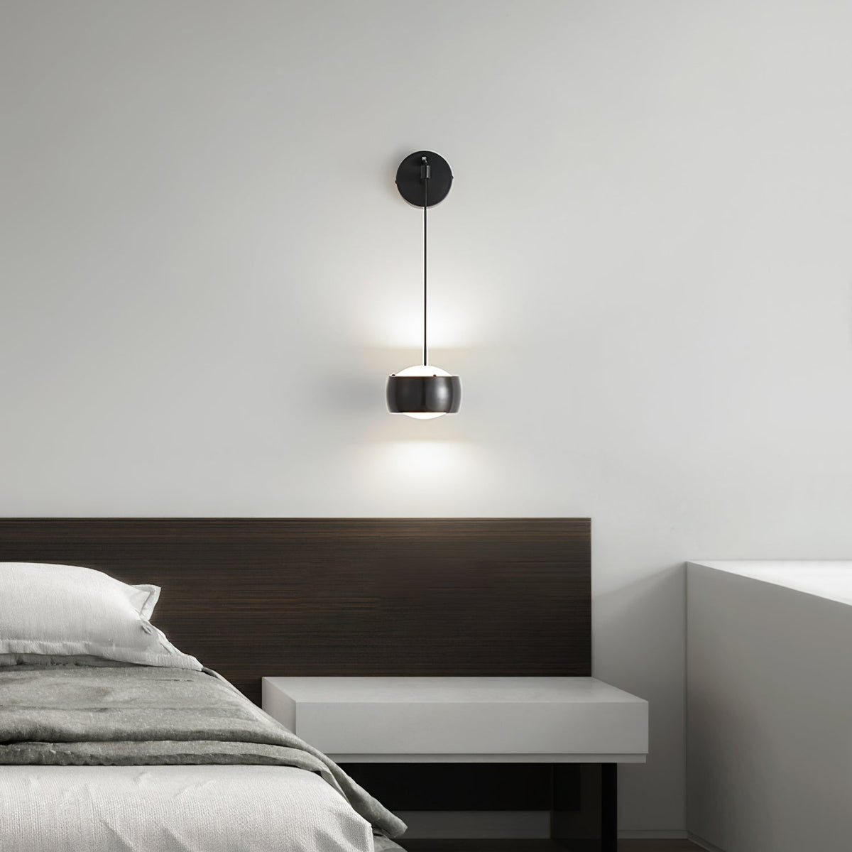 Lit black Clérachic wall light above a bed with a dark wood headboard and a pale floating bedside shelf.