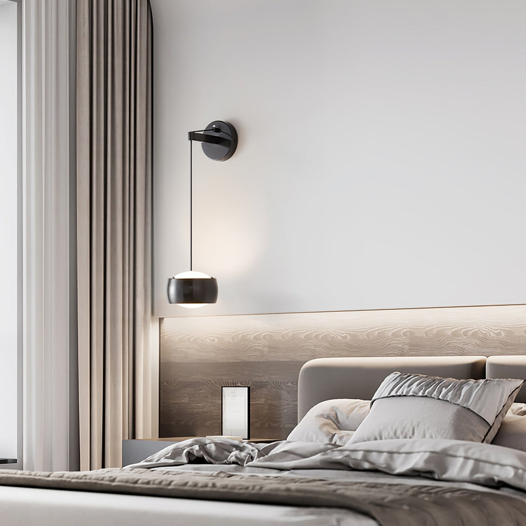 Black Clérachic wall light over a bed with grey linen and a lit wood-grain headboard panel, with a curtain at the left.