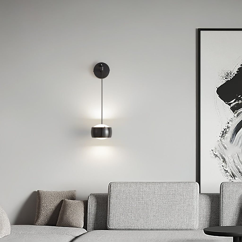 Lit black Clérachic wall light above a grey sofa, beside a large black and white abstract painting.