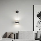 Lit black Clérachic wall light above a grey sofa, beside a large black and white abstract painting.