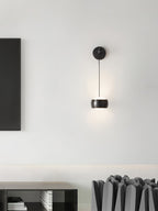 Black Clérachic wall light on a white wall beside a dark panel, with a low shelf and grey sculptural objects below.