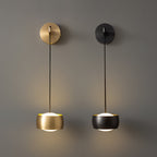 A brass Clérachic wall light and a black one side by side on a taupe wall, both lit from beneath their shades.