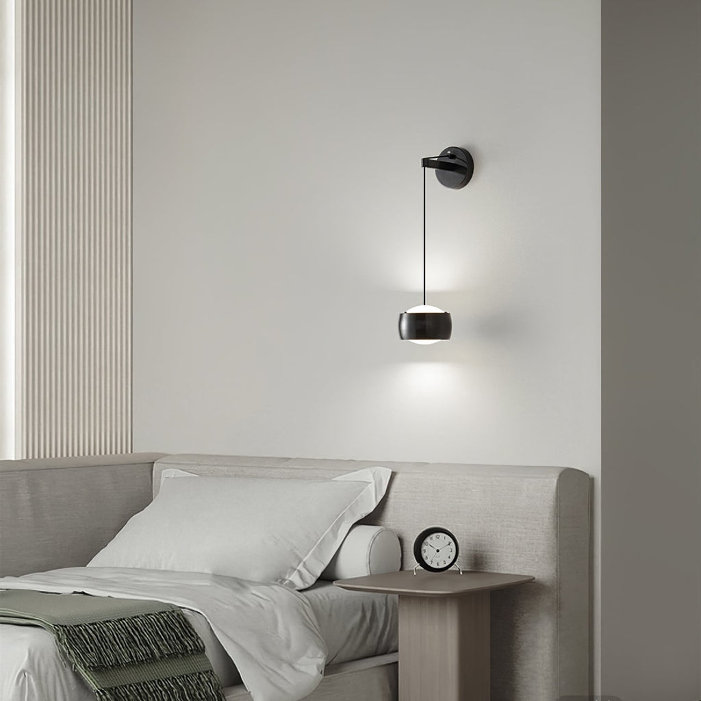 Lit black Clérachic wall light above a bed with cream linen and a small round clock on the bedside table.