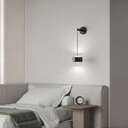 Lit black Clérachic wall light above a bed with cream linen and a small round clock on the bedside table.