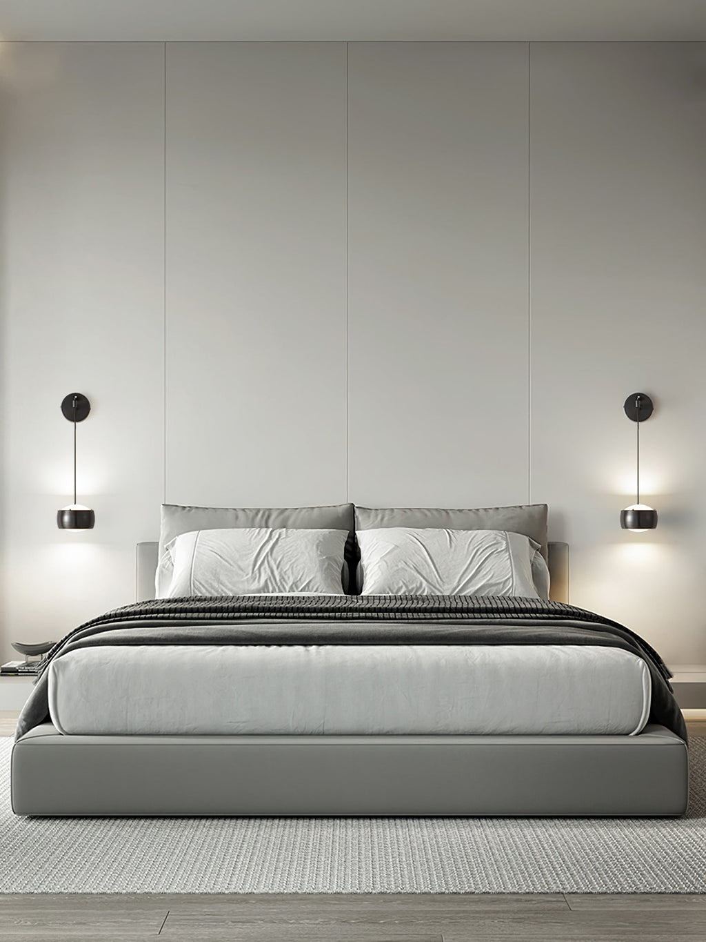 Pair of black Clérachic wall lights either side of a bed with grey bedding and a pale upholstered headboard.