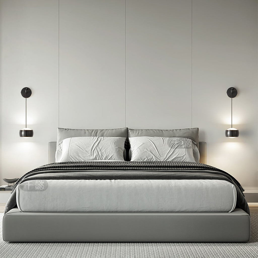 Pair of black Clérachic wall lights lit either side of a bed with grey bedding and a soft grey headboard wall.