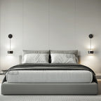 Pair of black Clérachic wall lights lit either side of a bed with grey bedding and a soft grey headboard wall.