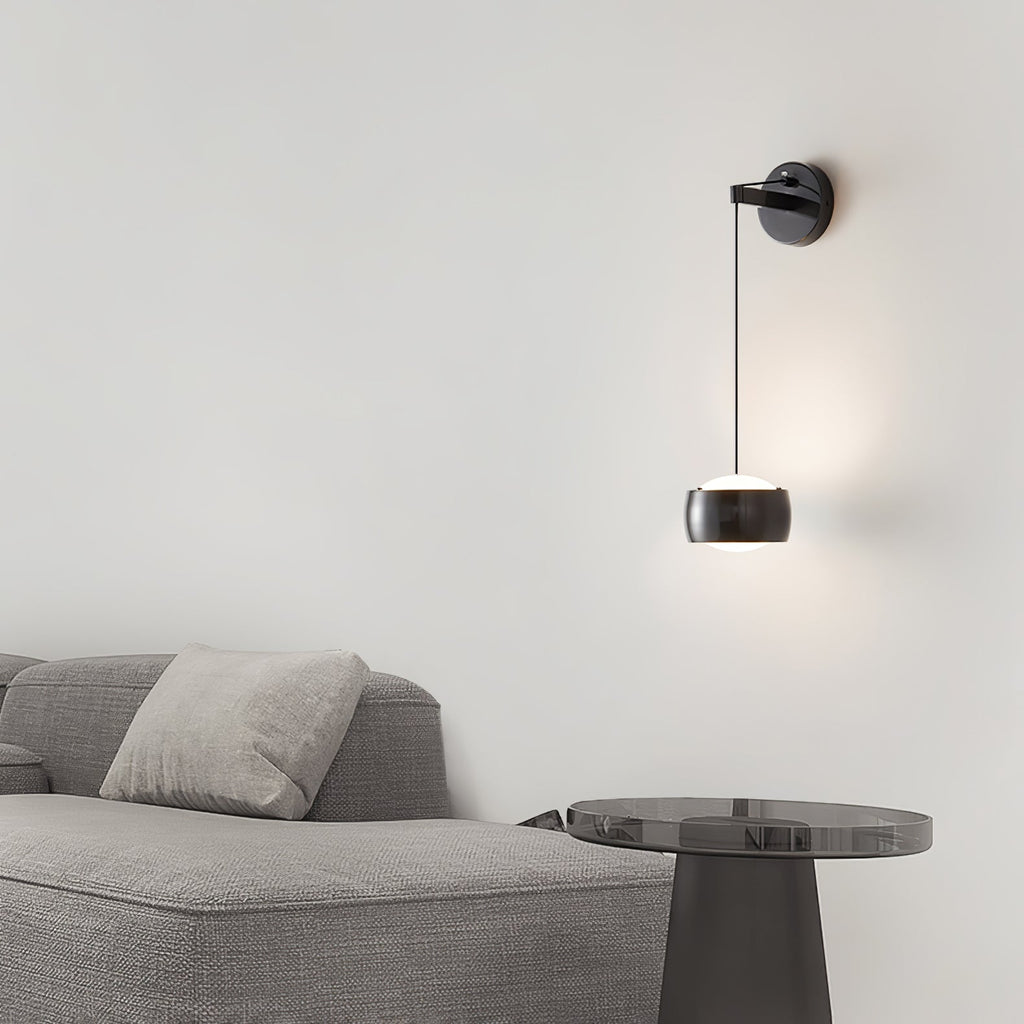 Black Clérachic wall light lit above a grey sofa, with a smoked-glass side table at the right.