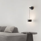 Black Clérachic wall light lit above a grey sofa, with a smoked-glass side table at the right.