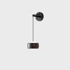 Black Clérachic wall light on a pale grey backdrop, its glossy cylinder shade with a white diffuser below a round backplate.