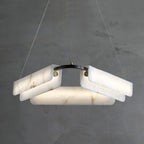 The three-head Clérachic Delia chandelier lit against a concrete wall, stone panels glowing above the central diffuser.