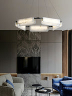 Clérachic Delia chandelier lit in a living room with a stone fireplace, grey cabinetry and a blue velvet armchair.