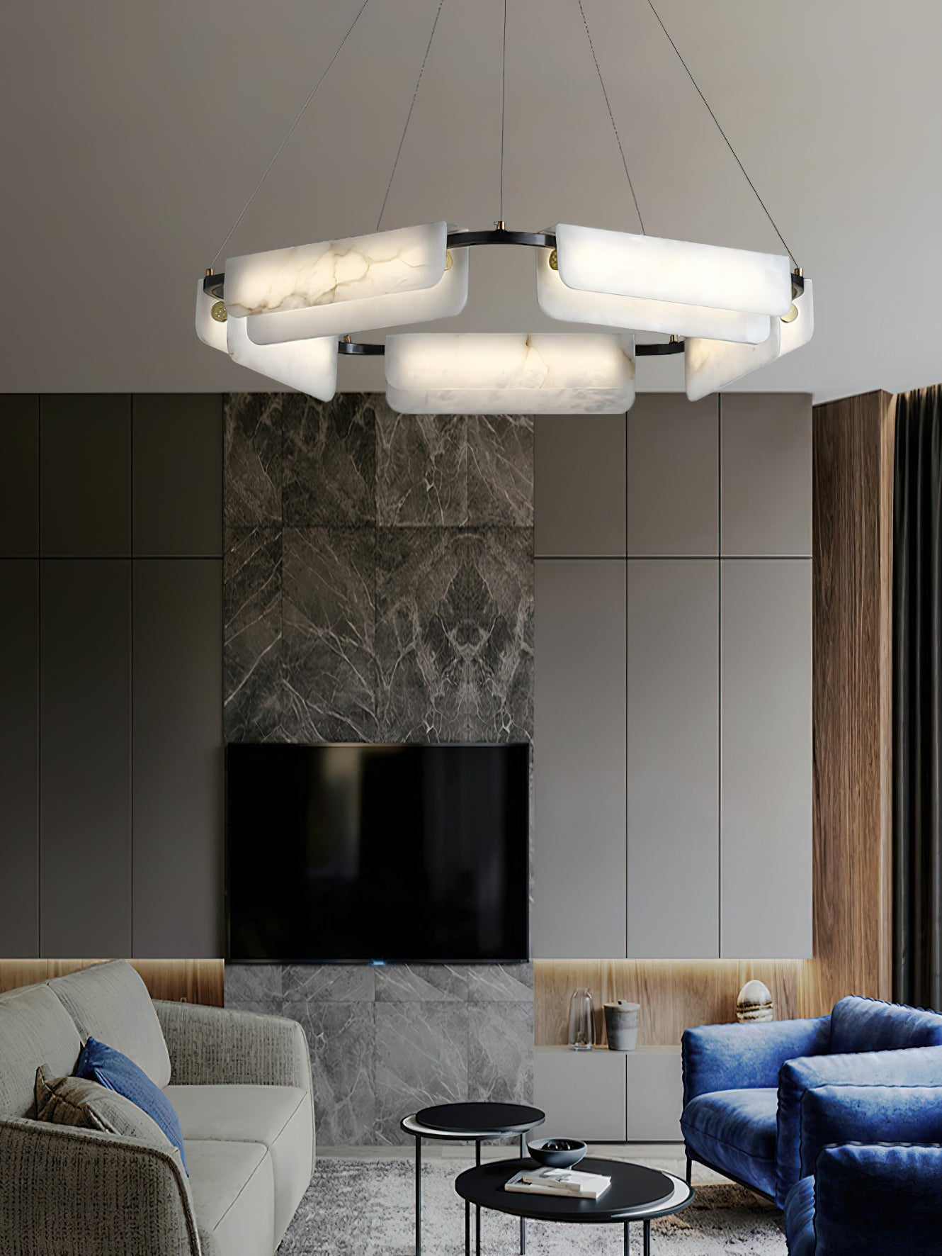 Clérachic Delia chandelier lit in a living room with a stone fireplace, grey cabinetry and a blue velvet armchair.