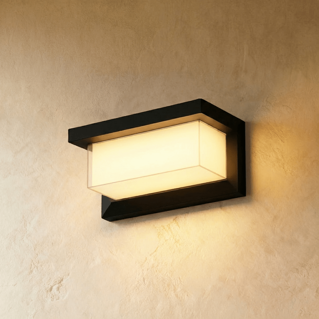 Clérachic black horizontal outdoor wall lamp with a frosted rectangular diffuser, glowing warm white on a limewashed wall