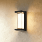Clérachic tall black outdoor wall lamp with an open-sided frame and a glowing white diffuser, lighting a plaster wall