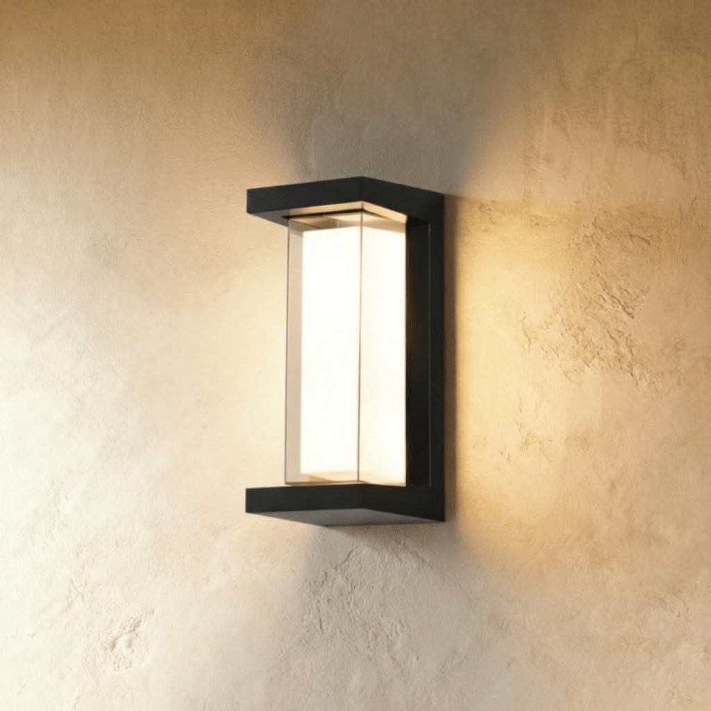 Clérachic tall black outdoor wall lamp with an open-sided frame and a glowing white diffuser, lighting a plaster wall