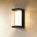 Clérachic tall black outdoor wall lamp, larger size, with an open-sided frame and a lit white diffuser on plaster