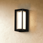 Clérachic larger black framed outdoor wall lamp with a glowing white diffuser, mounted high on a plaster wall
