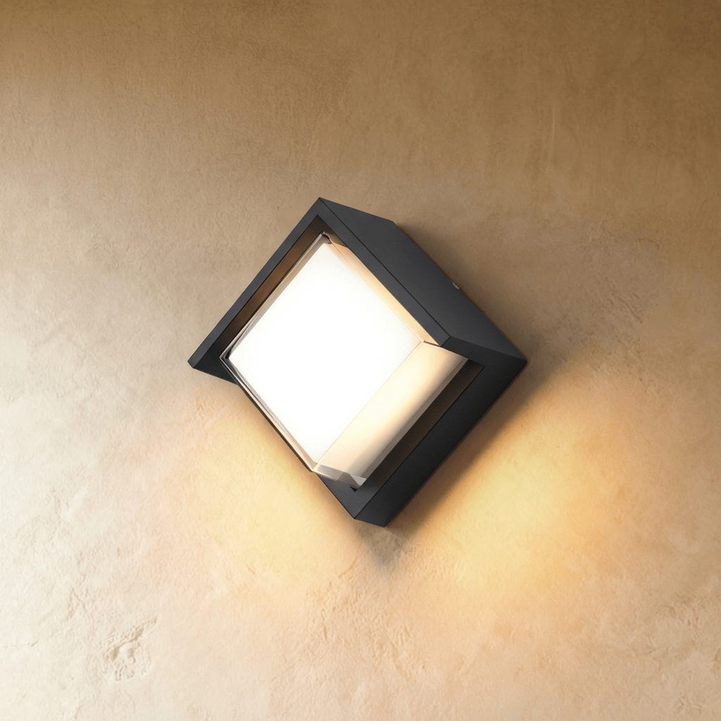 Clérachic compact black outdoor wall lamp with a square-set diffuser tilted on the diagonal, lit warm white on a wall