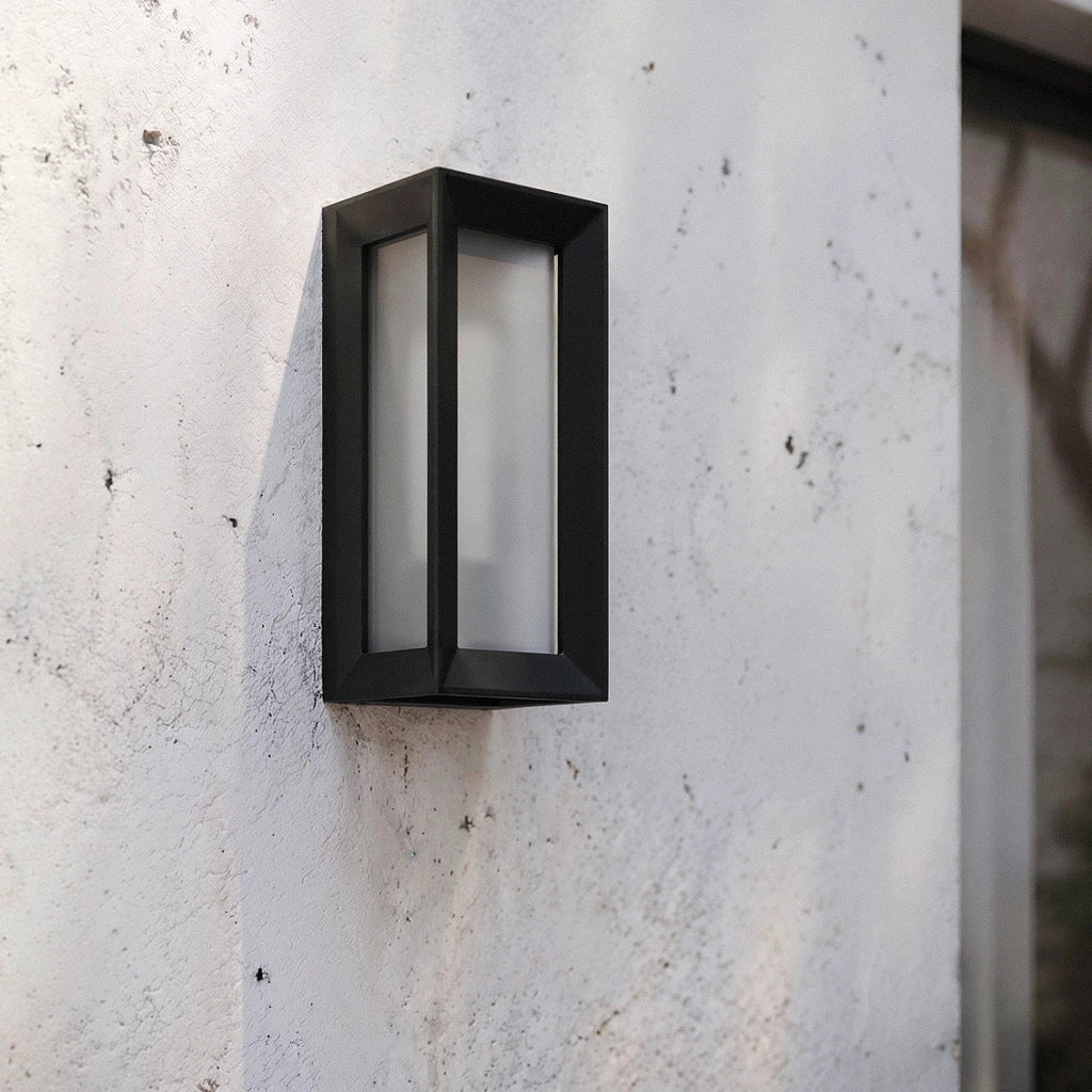 Clérachic black framed outdoor wall lamp with a frosted diffuser mounted on a rough white rendered exterior wall