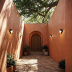 Clérachic compact black outdoor wall lamps glowing along terracotta courtyard walls on either side of an arched wooden door