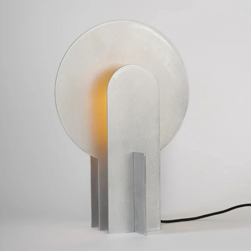 Clérachic disc-and-slab table lamp seen from an angle, showing the two upright plates that carry the disc, the narrow fin set at a right angle to the front slab, and the black cord trailing away.