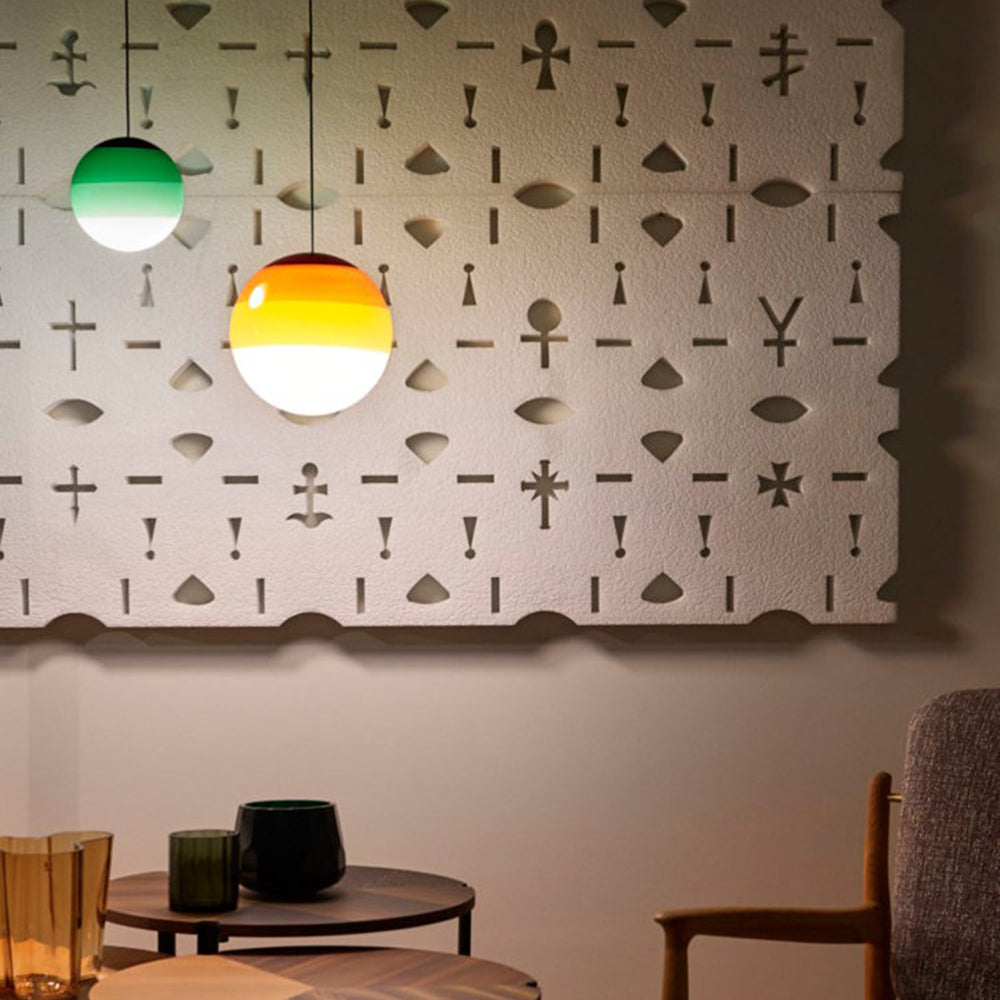 Green and amber Clérachic dipped gradient glass pendant lights lighting a lounge corner beside a carved wall panel.