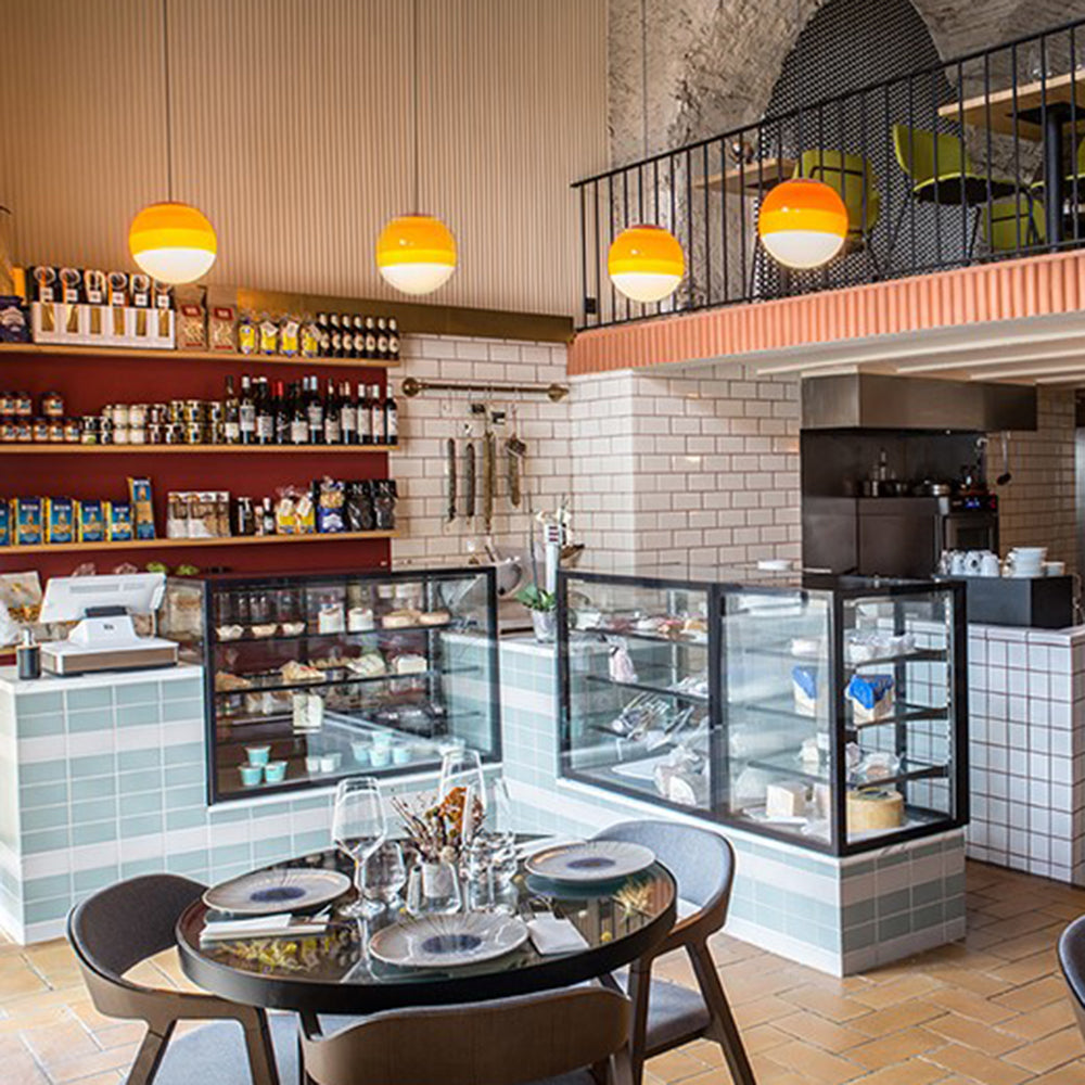 Four amber Clérachic dipped gradient glass pendant lights lighting the counter of a tiled deli café.