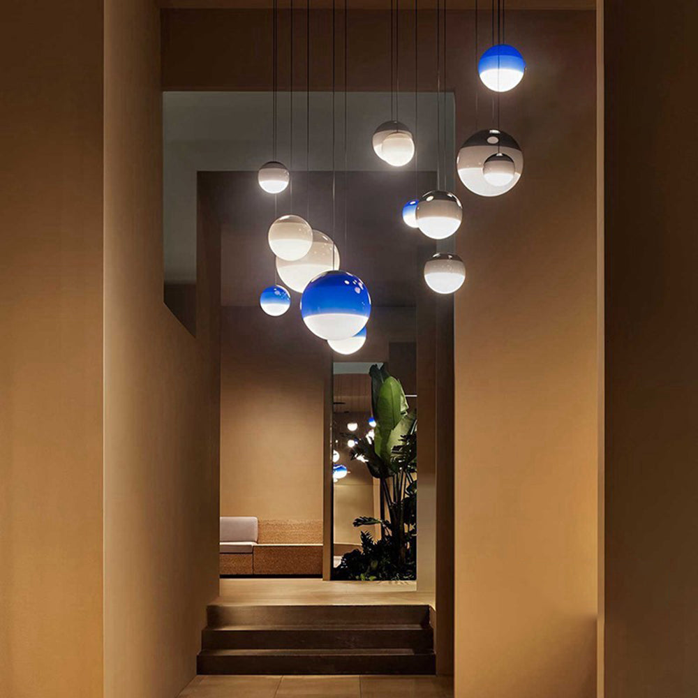 A cluster of blue and grey Clérachic dipped gradient glass pendant lights dropping at mixed heights over a stair hall.