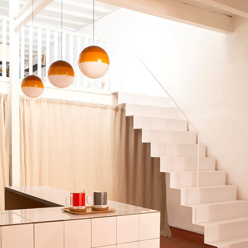 Three amber Clérachic dipped gradient glass pendant lights in a row above a tiled kitchen counter.