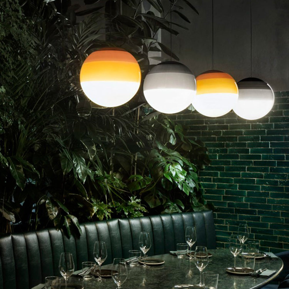 Amber and grey Clérachic dipped gradient glass pendant lights over a banquette table against a green brick wall.