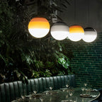 Amber and grey Clérachic dipped gradient glass pendant lights over a banquette table against a green brick wall.