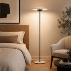 Lit softly beside a bed with a wooden headboard, a Clérachic floor lamp stands near a cream armchair and a potted tree.