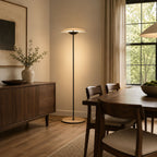 A Clérachic floor lamp lights a dining corner, with a walnut sideboard, a wooden table and linen curtains by a tall window.