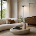 A Clérachic floor lamp stands behind a curved cream sofa and a stone coffee table, with an olive branch in a tall vase.