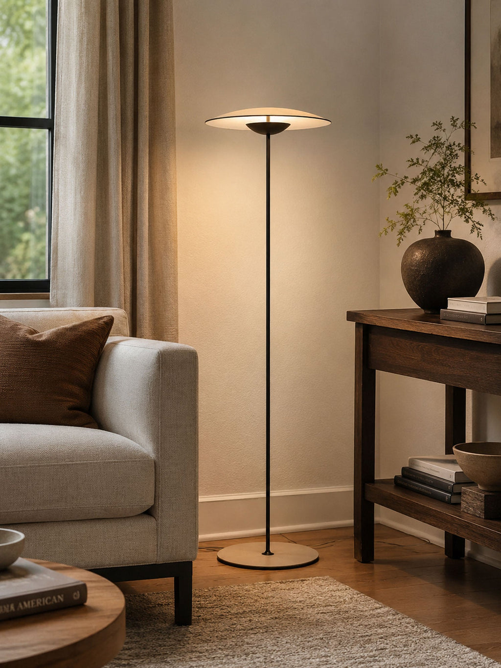 Warm light from a Clérachic floor lamp falls on a linen armchair and a wooden console with a dark vase.