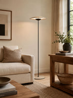 A Clérachic floor lamp rises behind a cream armchair and a small wooden side table, with a woven basket below.