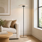 A Clérachic floor lamp stands in a bright corner by a window, beside a cream sofa, cushions and a round fluted coffee table.