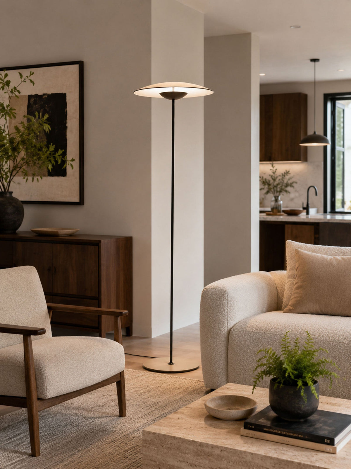 A Clérachic floor lamp stands in an open living room beside a cream sofa and a wooden armchair, with a plant on the table.