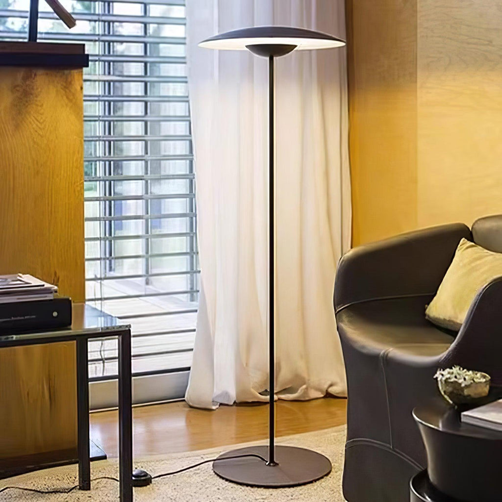 A matte black Clérachic floor lamp stands by sheer curtains and a leather armchair, its black cord running across the rug.