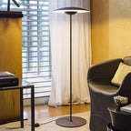 A matte black Clérachic floor lamp stands by sheer curtains and a leather armchair, its black cord running across the rug.