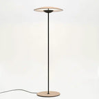 This Clérachic floor lamp on a pale backdrop, its wood-grain disc shade lit from within and its black cord curving left.