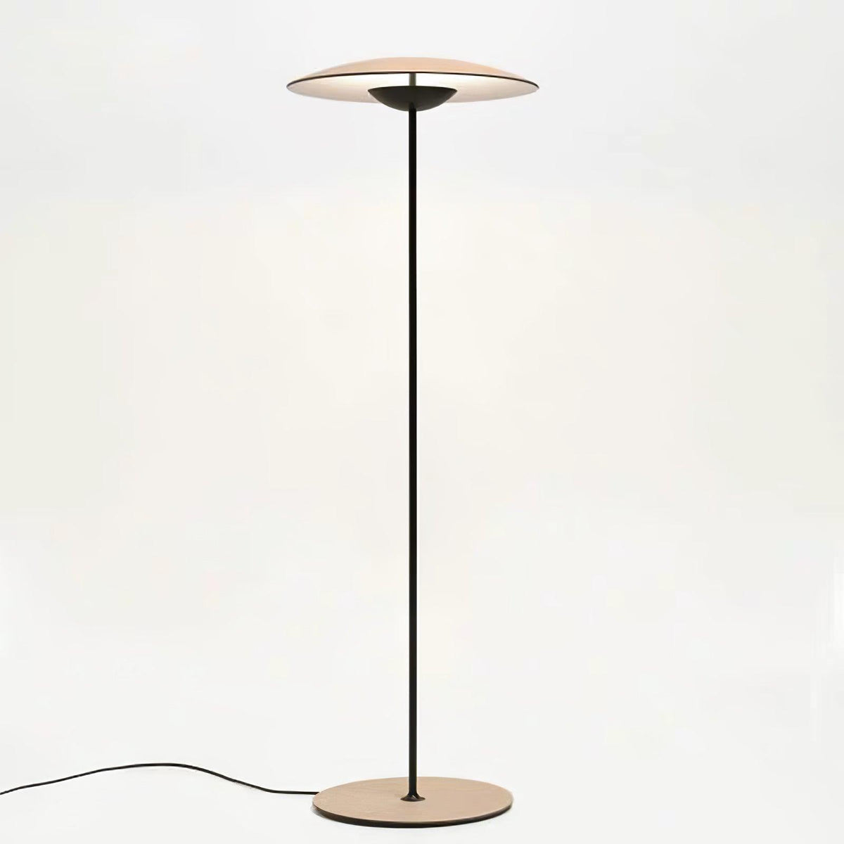 This Clérachic floor lamp on a pale backdrop, its wood-grain disc shade lit from within and its black cord curving left.