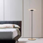 Beside a low bed with a dark headboard, this Clérachic floor lamp stands against pale panelled doors.