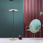 A Clérachic floor lamp stands against a teal wall and a pink pleated curtain, beside a pale-blue round-backed chair.