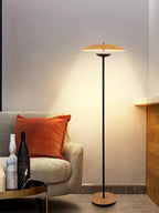 A Clérachic floor lamp casts a warm glow over a cream armchair with an orange cushion and marble vases on a side table.