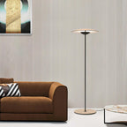 A Clérachic floor lamp stands in front of a ribbed wall beside a brown sofa with a striped cushion and a marble table.