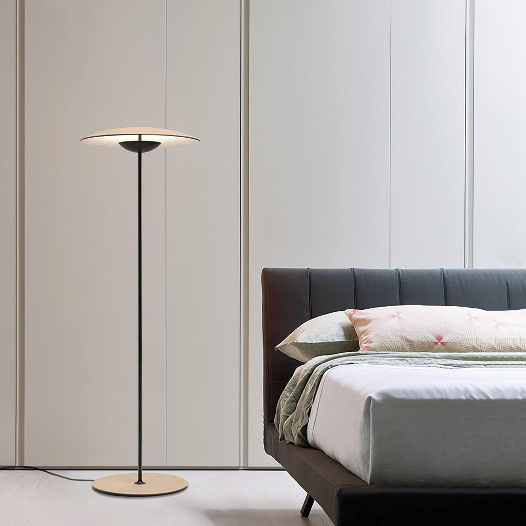 A Clérachic floor lamp stands beside a bed with a grey ribbed headboard and sage-green bedding, in front of tall panels.
